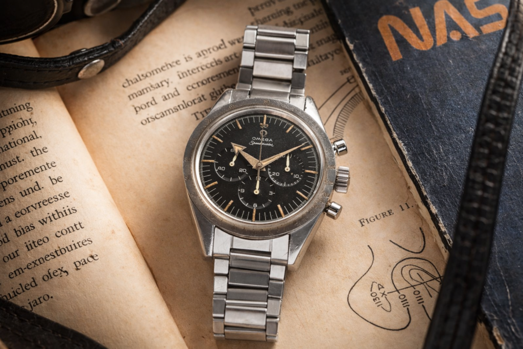Vintage-inspired stainless steel chronograph watch photographed on aged paper with books and leather accessories in warm natural light