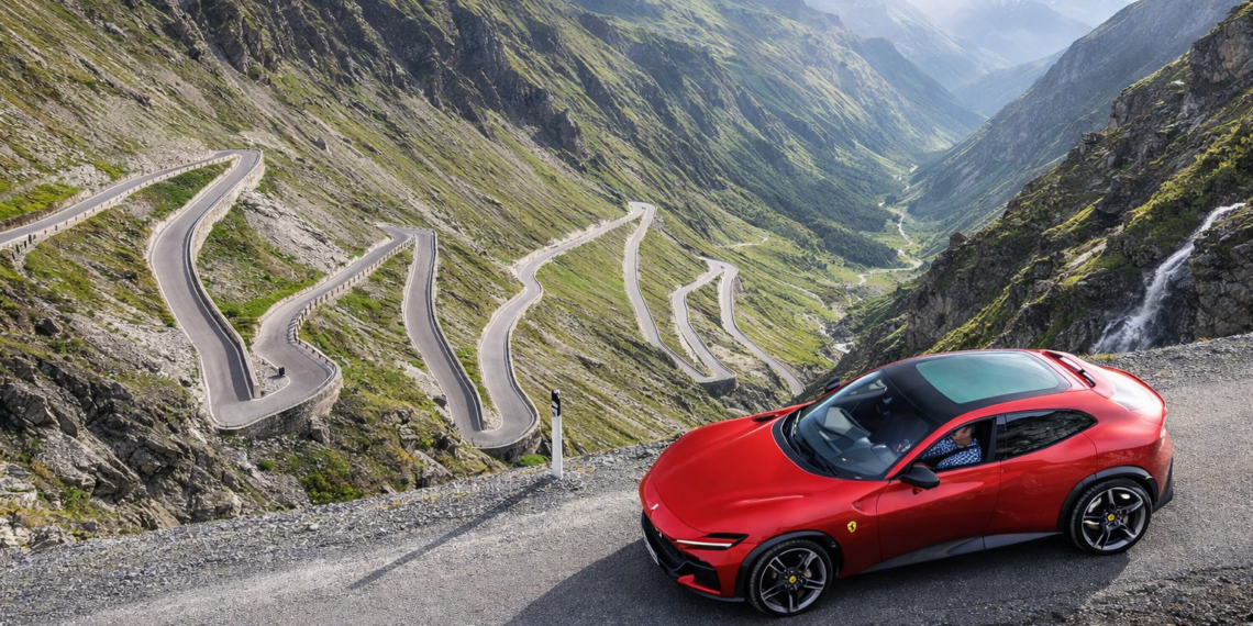 Red Ferrari-style luxury crossover parked on a dramatic alpine mountain road above a series of tight winding switchbacks and steep green valleys. Title: