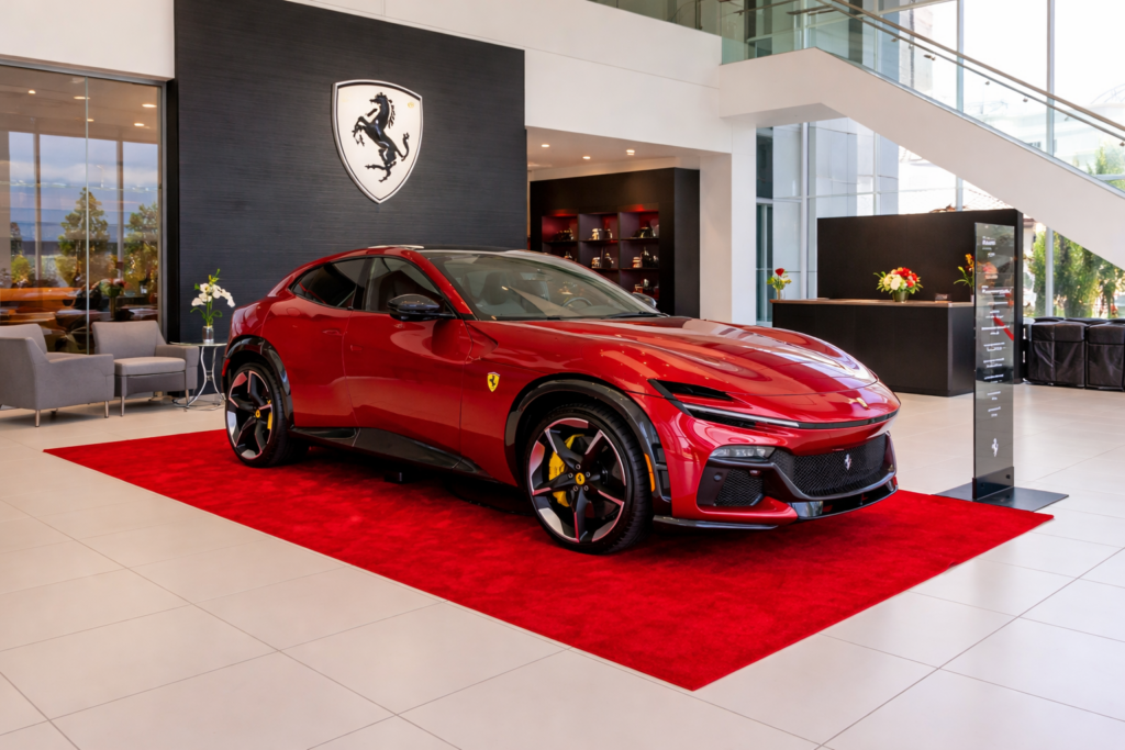 Red Ferrari Purosangue luxury SUV displayed on a red carpet inside a modern Ferrari showroom with glass architecture