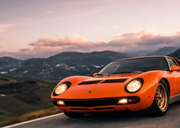 Orange Lamborghini Miura classic exotic supercar driving through scenic mountain road at sunset