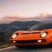Orange Lamborghini Miura classic exotic supercar driving through scenic mountain road at sunset