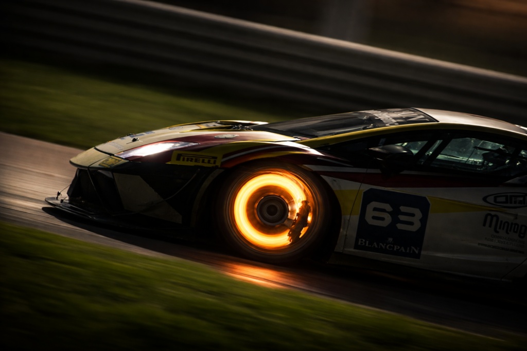 Glowing brake disc on GT3 race car during high-speed night endurance racing with intense heat and motion blur
