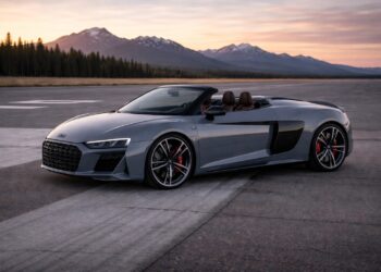 Metallic gray Audi R8 Spyder parked on an open runway at sunset with mountains and a pine tree backdrop