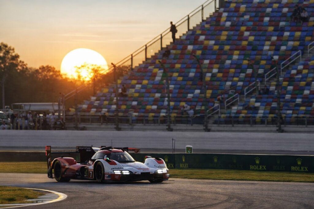 LMDh race car driving through a corner at sunset with grandstands in the background