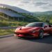 Red exotic supercar driving past solar panel farm on scenic highway