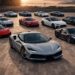 Hybrid and electric exotic supercars including Ferrari SF90, McLaren Artura, and luxury EV hypercars lined up at sunset overlooking a coastal landscape