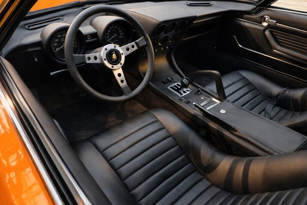 Interior of an orange Lamborghini Miura with black leather seats and gated manual shifter