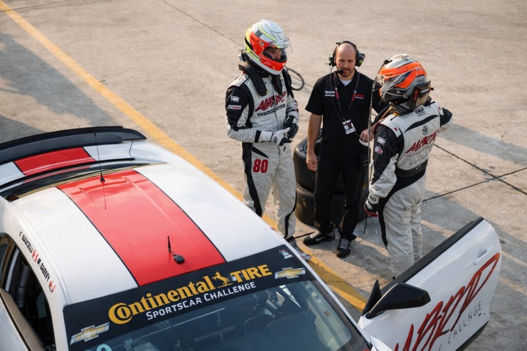 race car drivers and crew discussing strategy in motorsports paddock beside race car