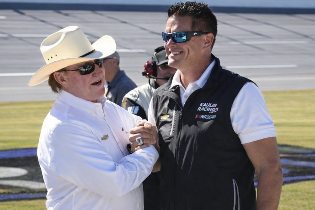 two motorsports executives shaking hands trackside at a NASCAR event during daytime