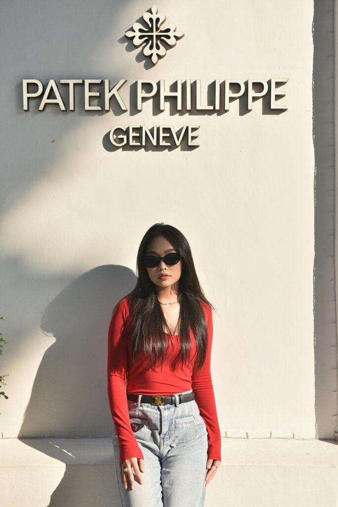 Woman in red top and sunglasses standing against a wall with luxury watch brand signage in bright daylight