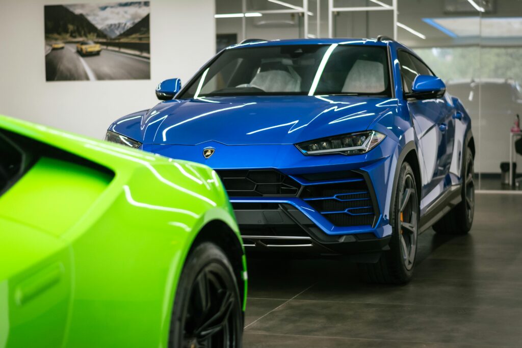 Blue Lamborghini Urus in a modern showroom with a bright green Lamborghini partially visible in the foreground.