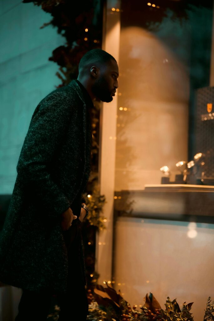 Man in a dark overcoat looking into a luxury watch boutique window display at night