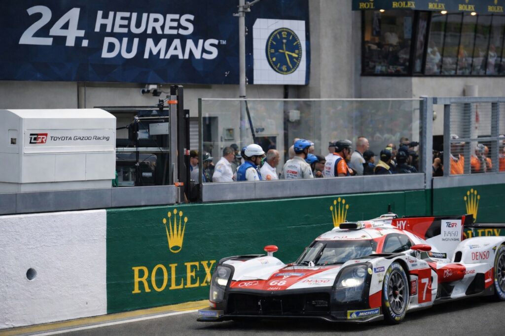 Toyota Gazoo Racing Le Mans Hypercar exiting pit lane during an endurance racing session with Rolex-branded barriers in the background.