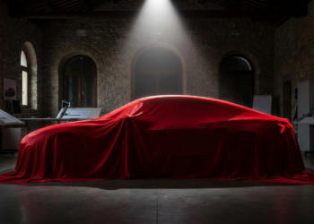 Silhouette of a four-door electric grand tourer beneath a red silk cover in a design studio