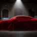 Silhouette of a four-door electric grand tourer beneath a red silk cover in a design studio