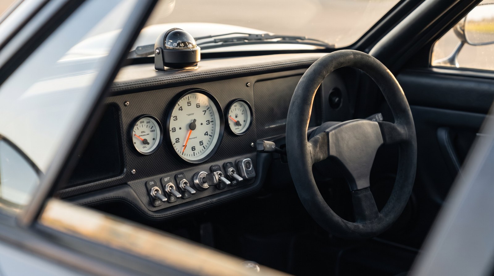 Minimalist supercar cockpit with a large central analogue tachometer, toggle switches and no digital screens