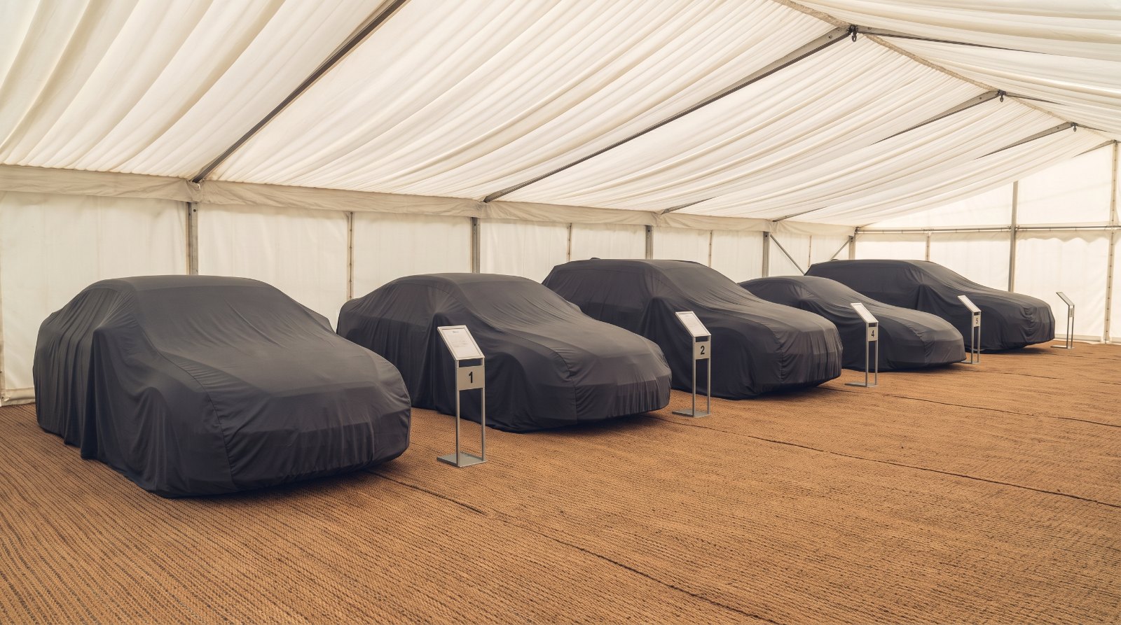 Row of cars under fitted grey covers in an auction holding tent before a preview