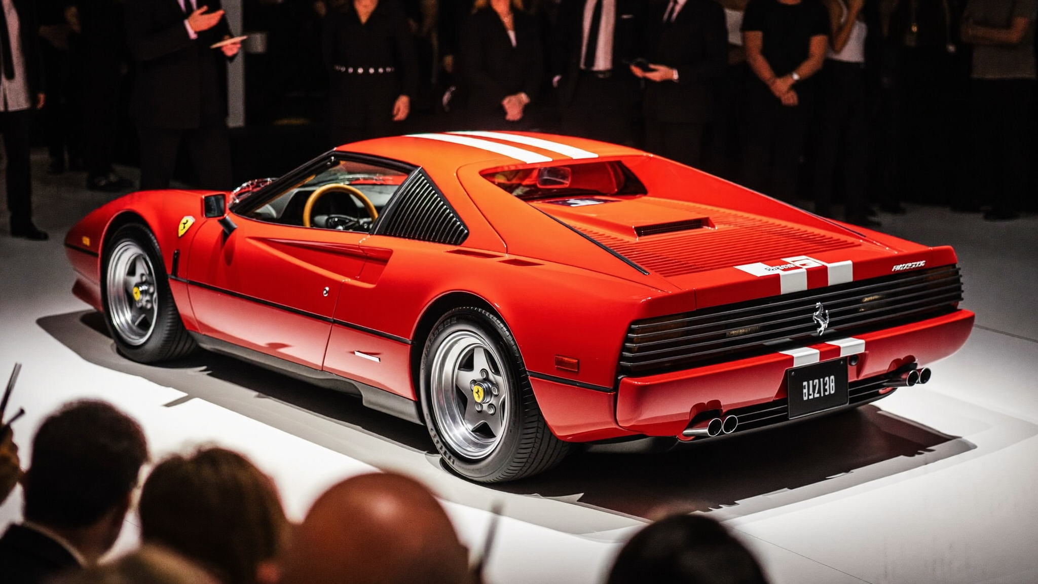 Red Ferrari crossing a spotlit collector car auction stage as bidders raise paddles at an evening sale