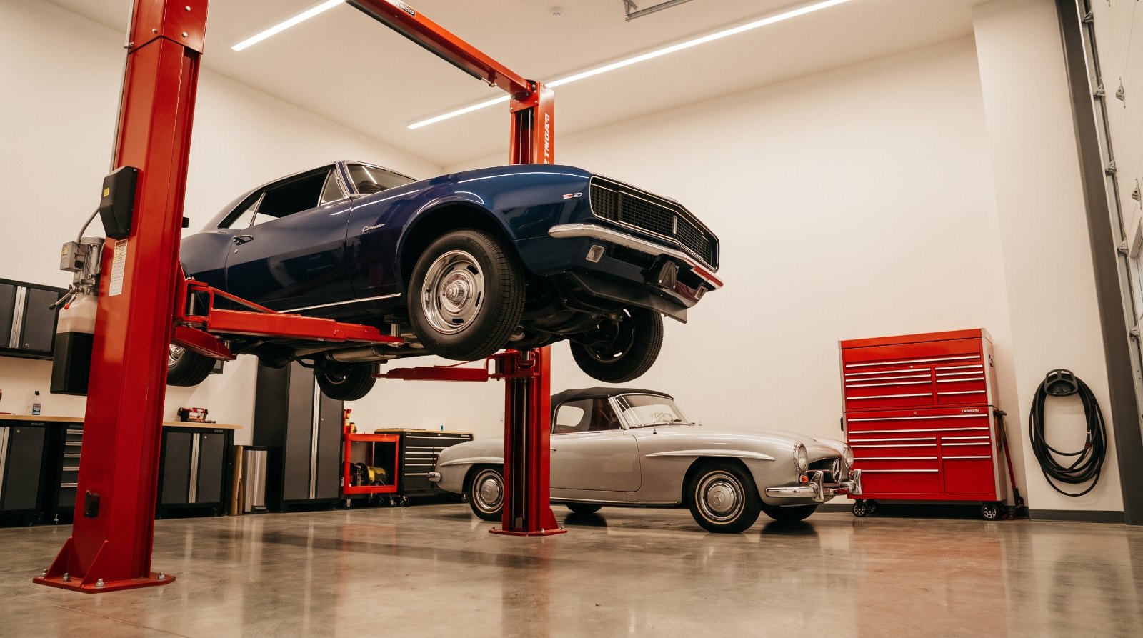 Classic muscle car raised on a red two-post hydraulic lift inside a private garage condo unit
