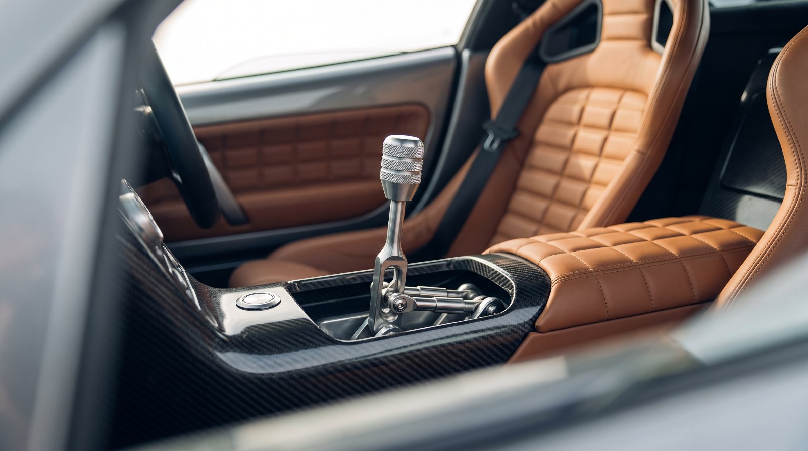 Knurled aluminium manual gear lever with exposed linkage and quilted leather, illustrating the McLaren McL 6GT cabin theme