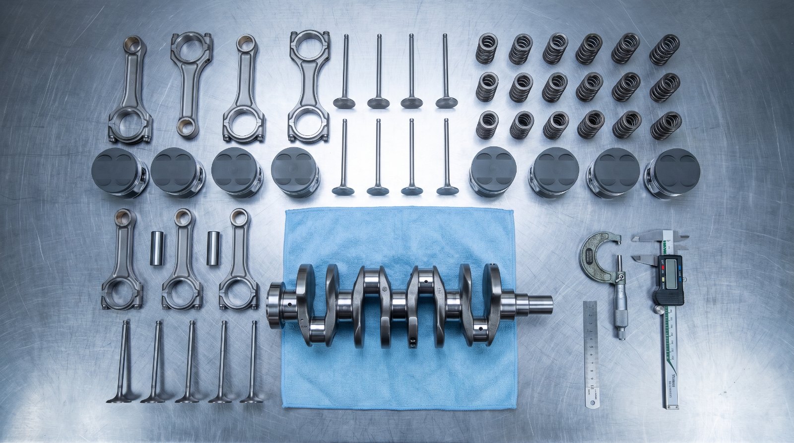 Titanium connecting rods, coated forged pistons and titanium valves laid out on a workbench with measuring tools