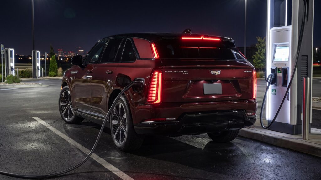 2026 Cadillac ESCALADE IQ rear three-quarter view plugged into a DC fast charger at night