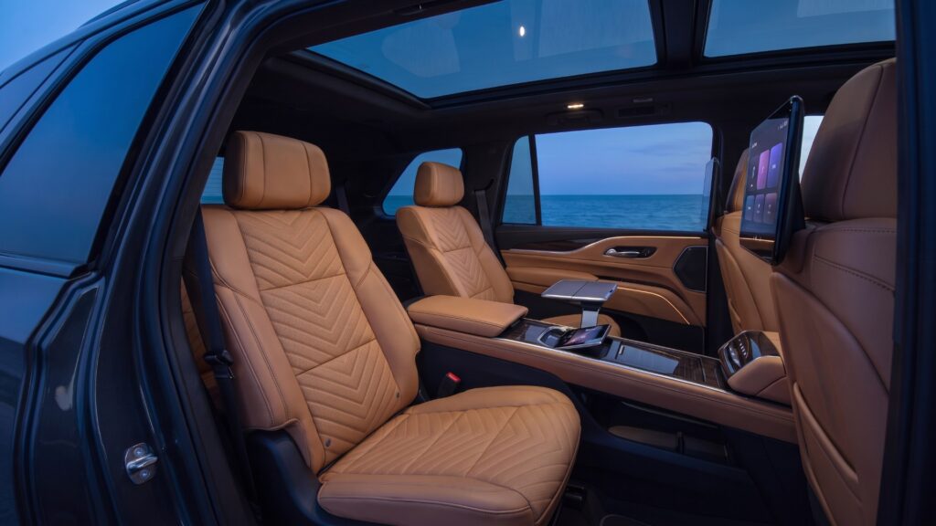 Illustration of the 2026 Cadillac ESCALADE IQ Executive Second Row captain’s chairs and center console, seen through the open rear door at blue hour