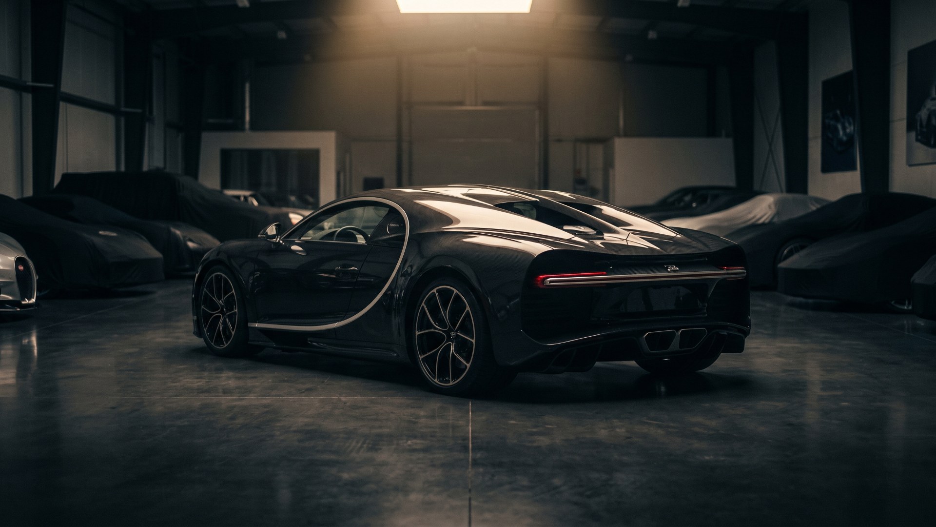 Black carbon Bugatti Chiron seen from the rear three-quarter in a dim private collection garage among covered cars. AI-generated editorial visualization, not a photograph.