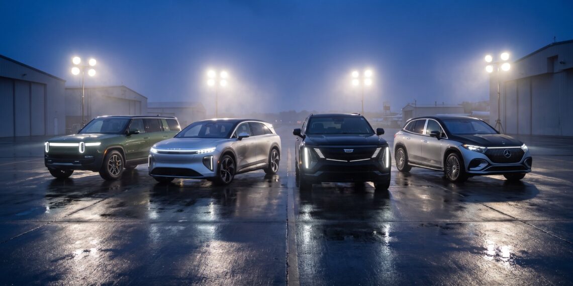 Four electric super-SUVs lined up with headlights on across a wet airfield apron at dusk: green Rivian R1S, silver Lucid Gravity, black Cadillac ESCALADE IQ and two-tone Mercedes-Maybach EQS SUV