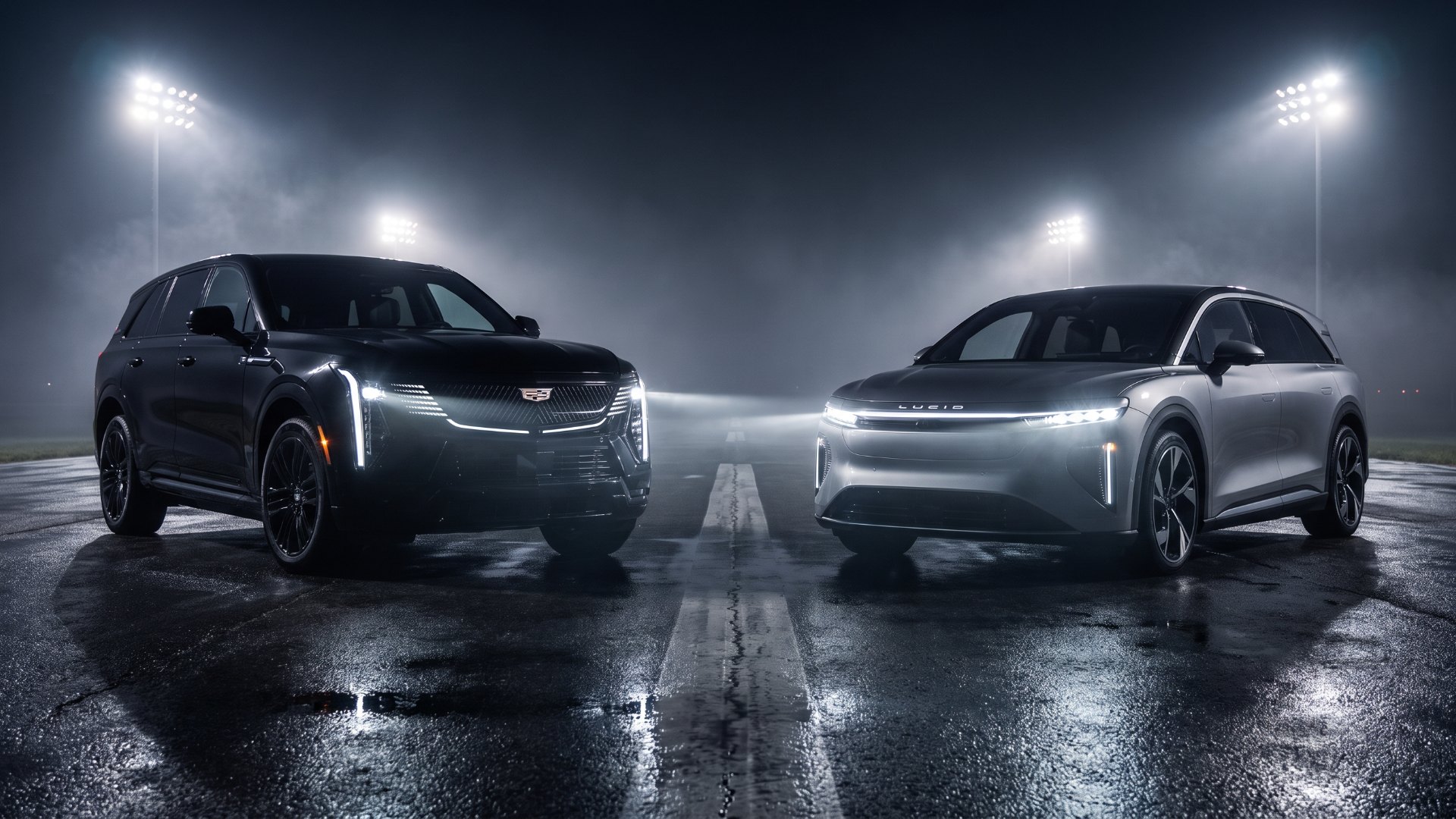 Electric super-SUV face-off: black Cadillac ESCALADE IQ and silver Lucid Gravity parked nose to nose on a wet runway at night under stadium floodlights and haze