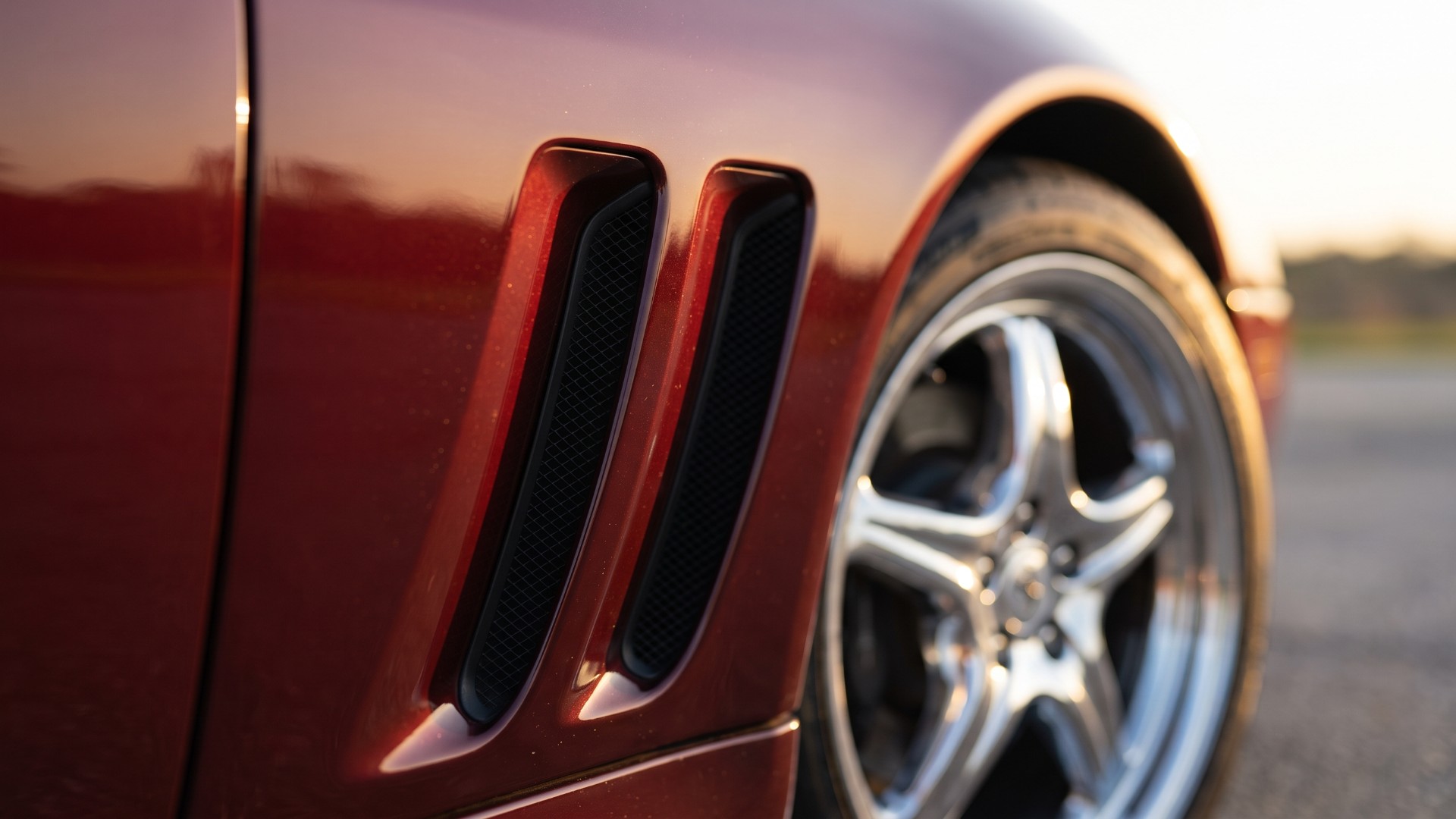 Close-up of the twin horizontal air outlet vents on the front fender of a dark red Ferrari 550 Maranello