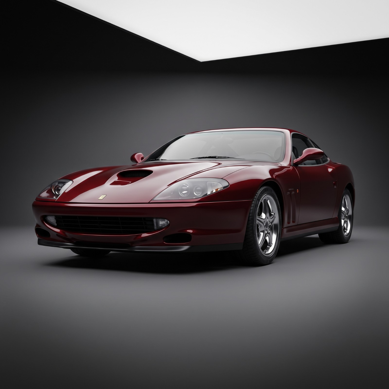 Studio-lit front three-quarter view of a dark red Ferrari 550 Maranello against a neutral dark background