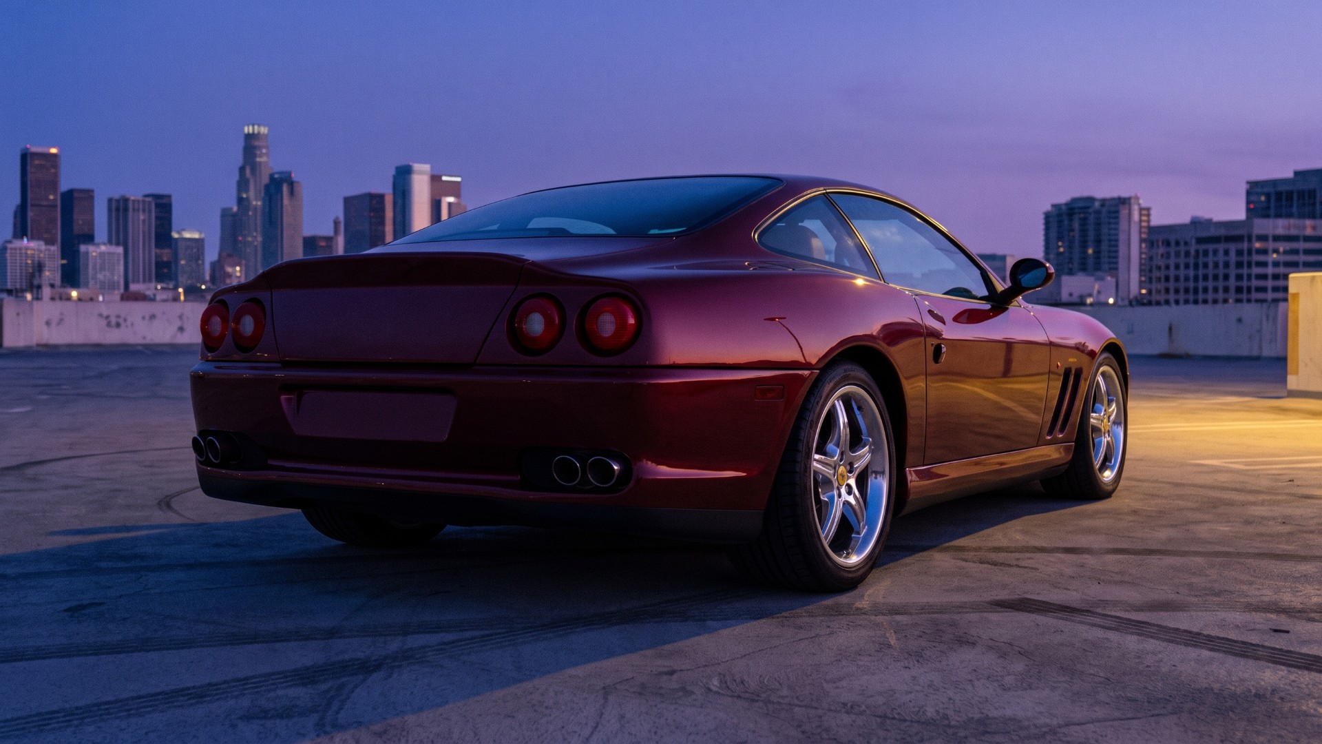 Rear three-quarter view of a dark red Ferrari 550 Maranello at dusk showing its four round taillights and twin exhaust outlets