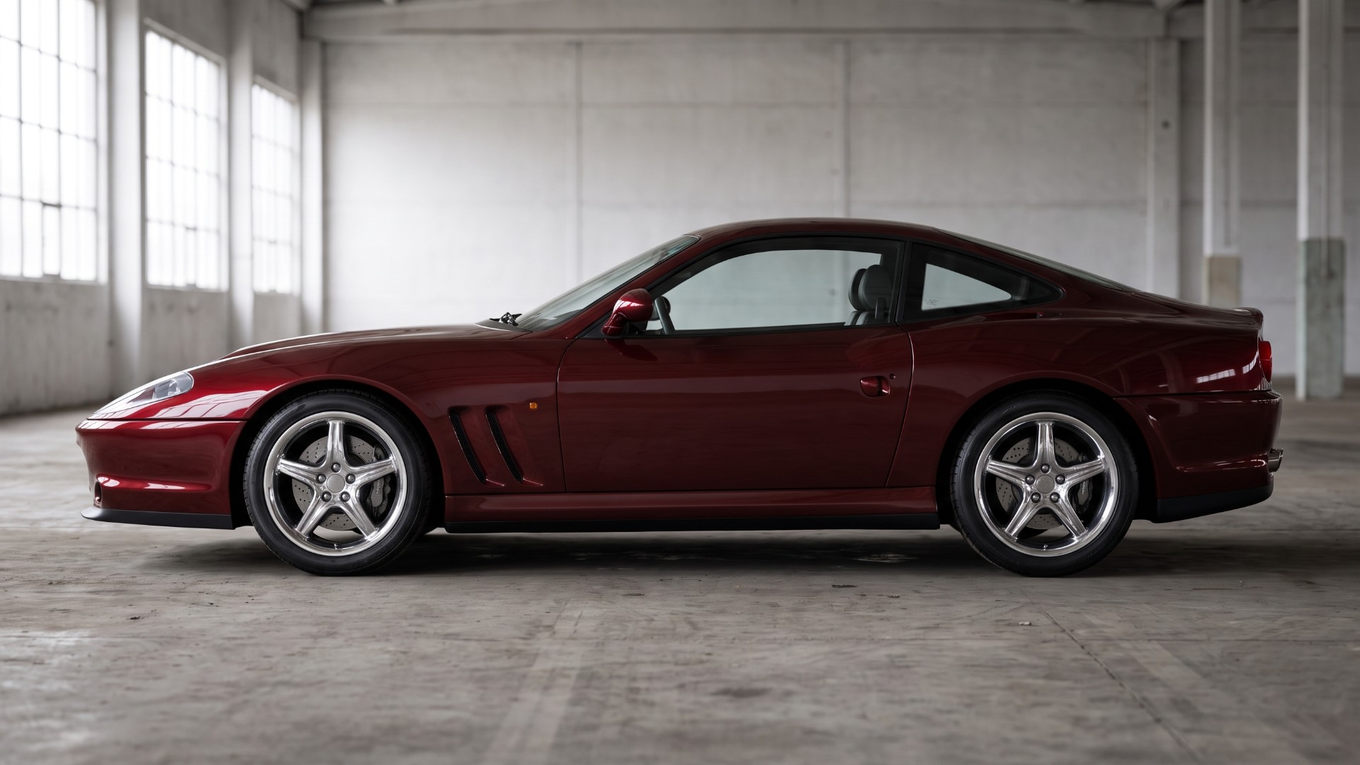 Side profile of a dark red Ferrari 550 Maranello showing the horizontal air outlet louvres set into the front fender