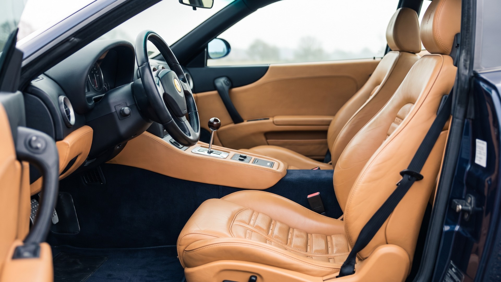 Tan leather interior of a left-hand-drive Ferrari 550 Maranello showing the open-gate six-speed manual shifter and pleated seats