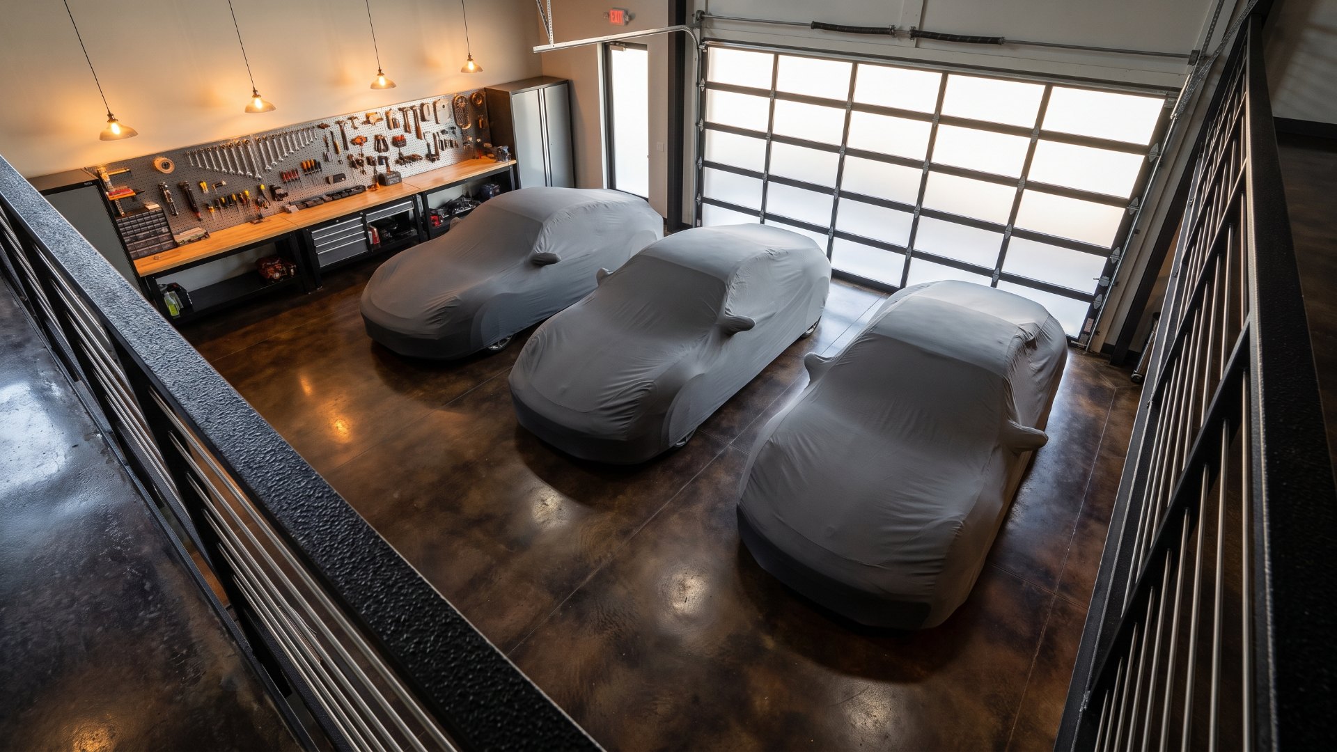 View from a garage condo mezzanine of three covered sports cars on a stained concrete floor