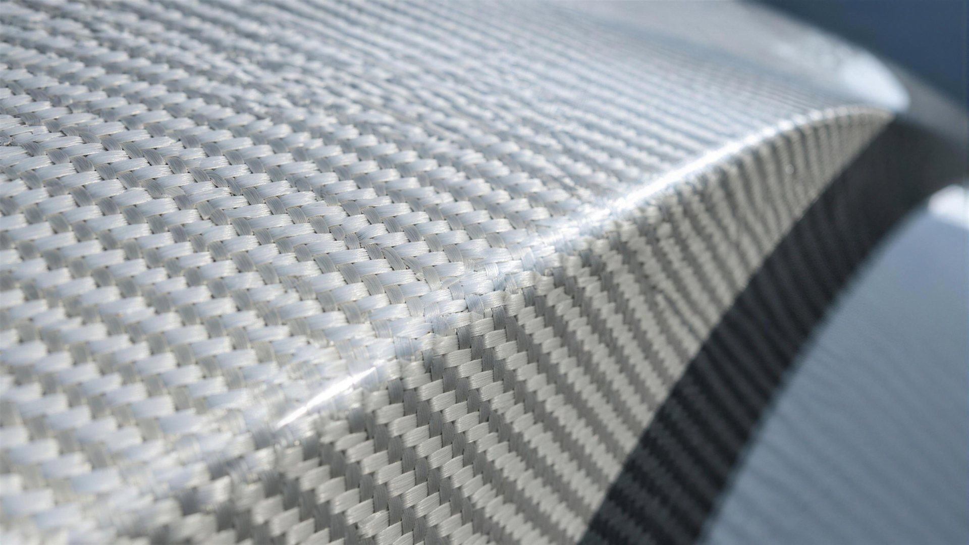 Macro detail of a white aramid and carbon composite body panel showing a woven twill pattern beneath clear lacquer