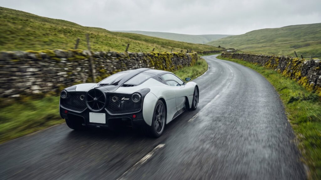 Silver Gordon Murray T.50 with its rear ground-effect fan visible, driving a narrow wet road between dry-stone walls