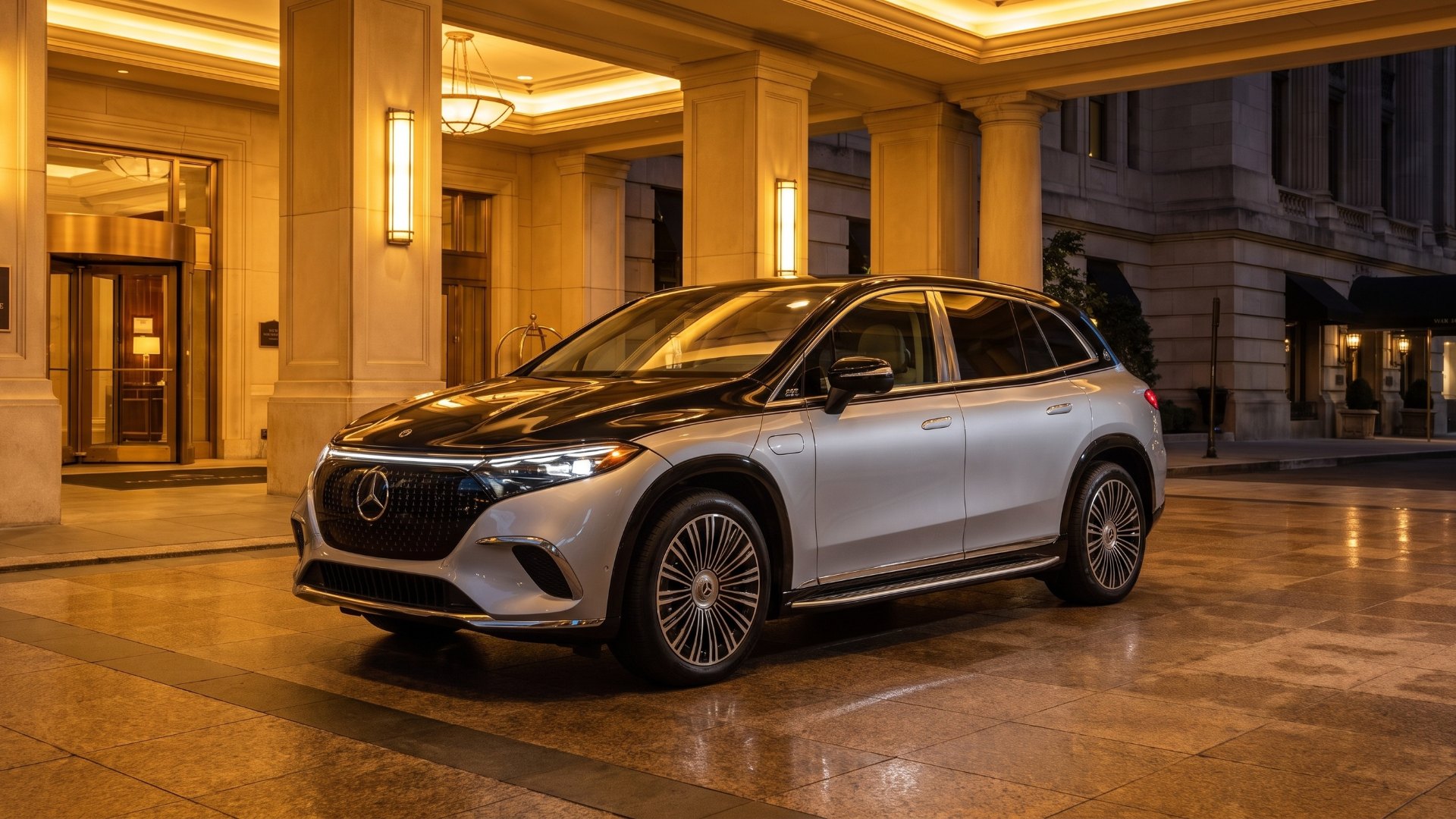 Two-tone black and silver Mercedes-Maybach EQS SUV parked under the lit entrance of a grand hotel at night