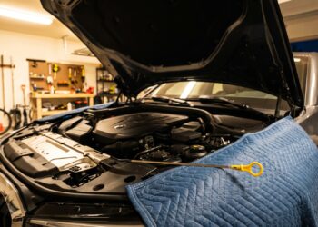 Modern sedan engine bay under plastic covers, with a loose oil dipstick resting on a fender cover