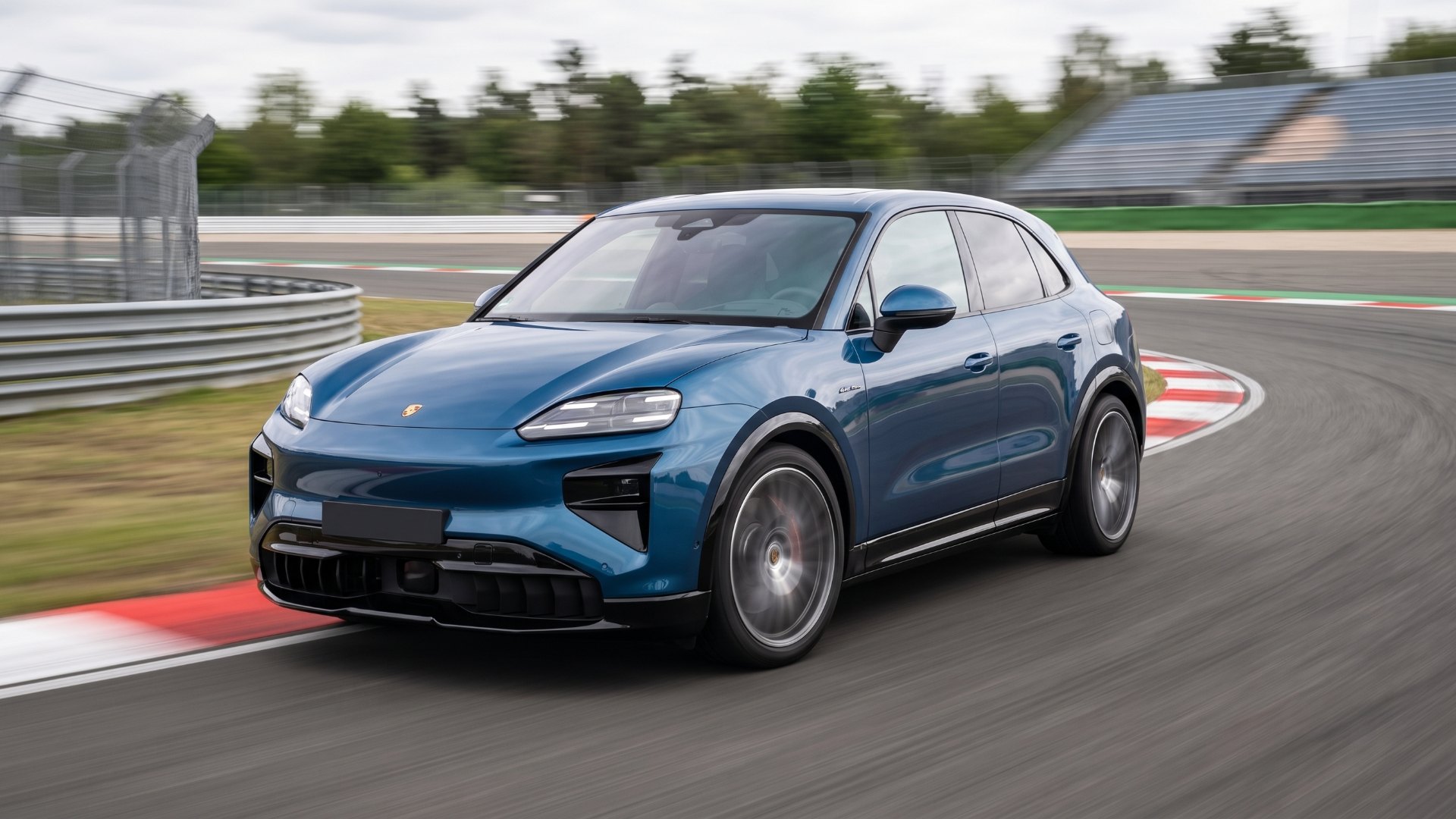 Blue Porsche Cayenne Turbo Electric cornering on a racetrack past red-and-white curbs