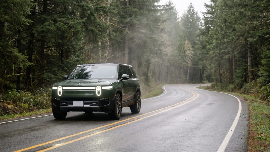Green Rivian R1S driving on a wet, clearly marked two-lane forest road