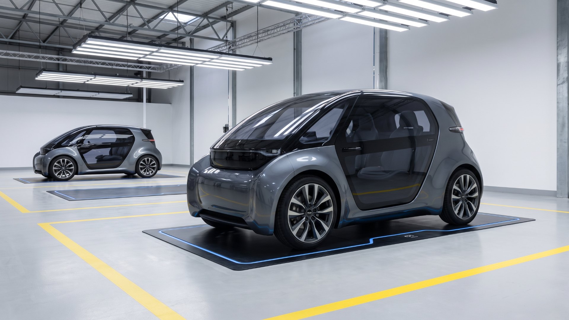 Driverless two-seat robotaxi parked over a flush wireless charging pad in a fleet depot bay