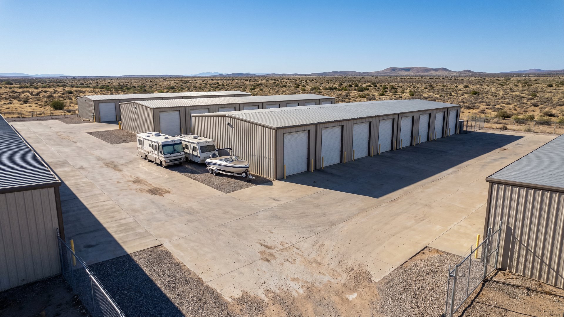 Plain metal storage condo buildings with white roll-up doors, an RV and a boat parked outside