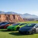 A row of modern supercars parked on manicured golf course fairway grass with red sandstone cliffs and the Spring Mountains behind them