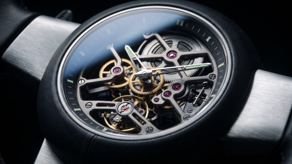 Close-up of a skeletonized watch-style instrument cluster with exposed gears and ruby jewels set in a steering wheel hub