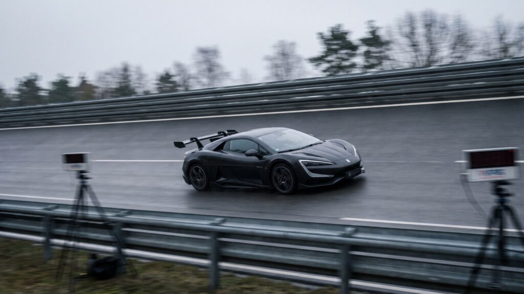 Black Yangwang U9 Xtreme electric hypercar at speed on a wet banked test track with timing equipment beside the barrier