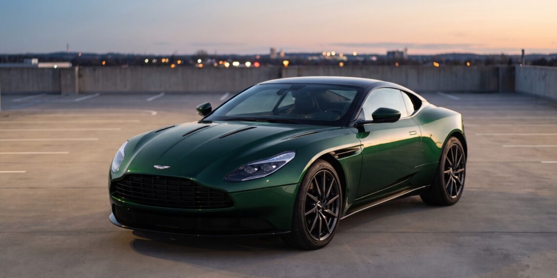 Dark green Aston Martin DB11 coupe parked on a rooftop parking deck at dusk