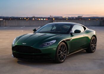 Dark green Aston Martin DB11 coupe parked on a rooftop parking deck at dusk