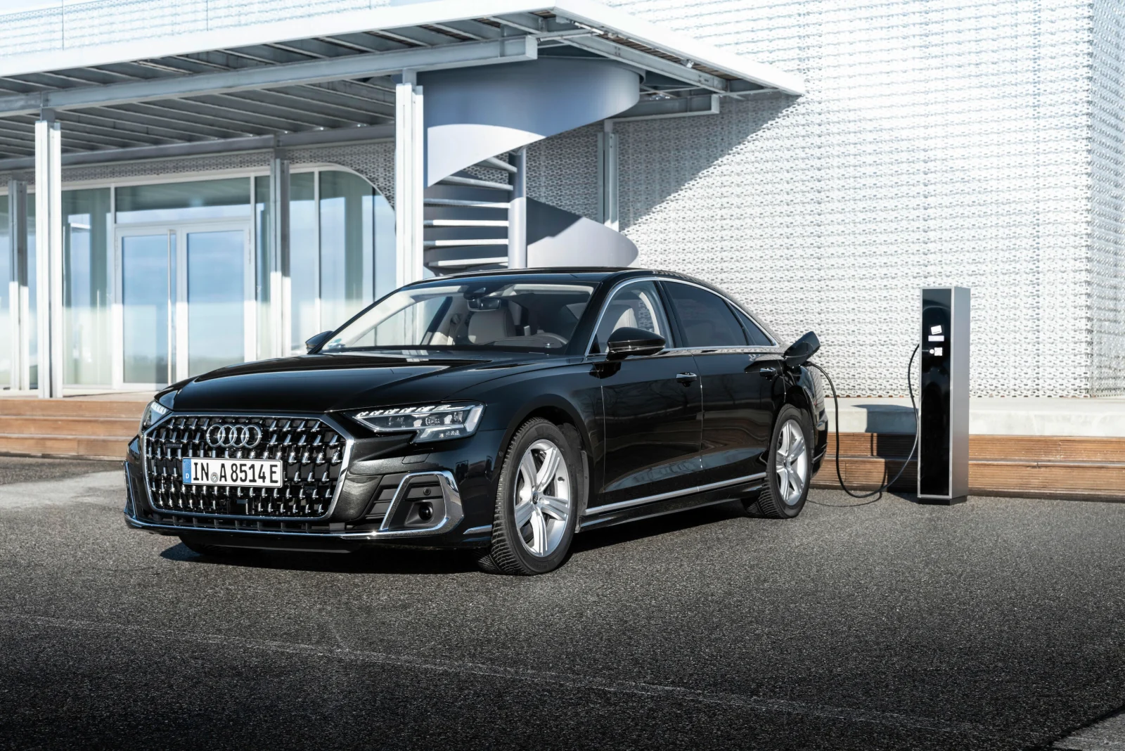 Black Audi A8 L sedan parked beside a modern building with a charging station